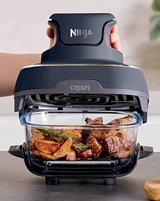 Image of the Ninja-Crispi-non-toxic-air-fryer full of food with woman lifting off the lid