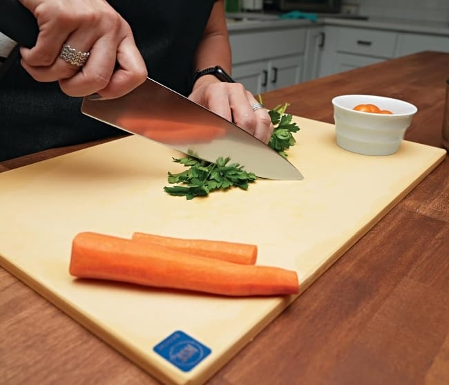 Man-slicing-carrots-and-greens-on-NoTrax-Natural-Rubber-Cutting-Board-on-wooden-countertop