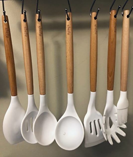 Image of Chefa USA wood and white silicone kitchen utensils hanging from utensil rack against beige wall background