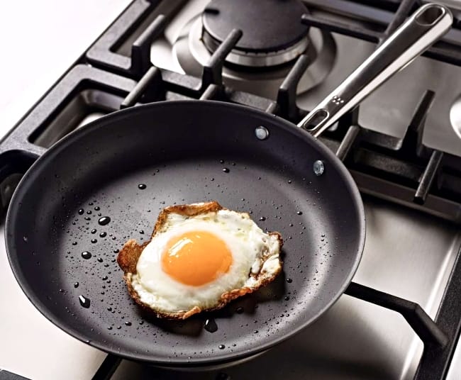 Image of a Misen Carbon Non-stick skillet on a gas stove with egg over easy sliding around inside the oiled pan