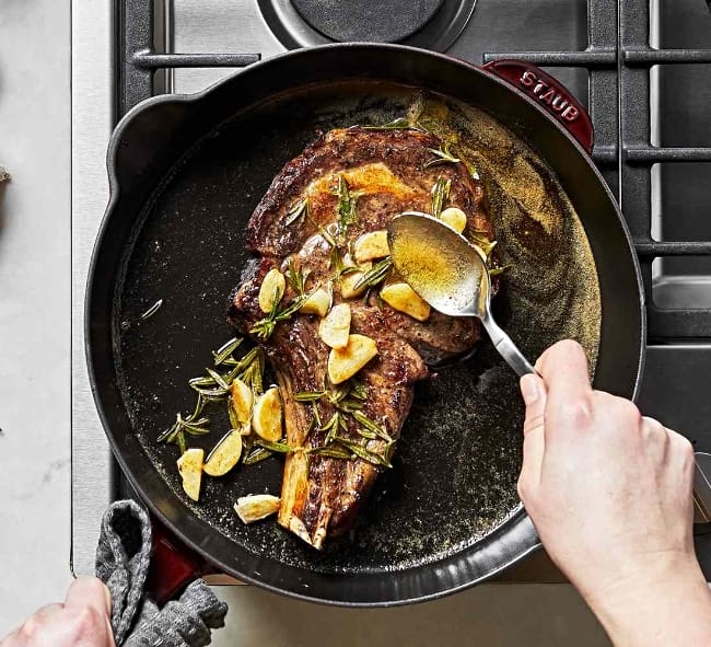 Image of a steak cooking in a Staub enameled cast iron skillet over a gas burner