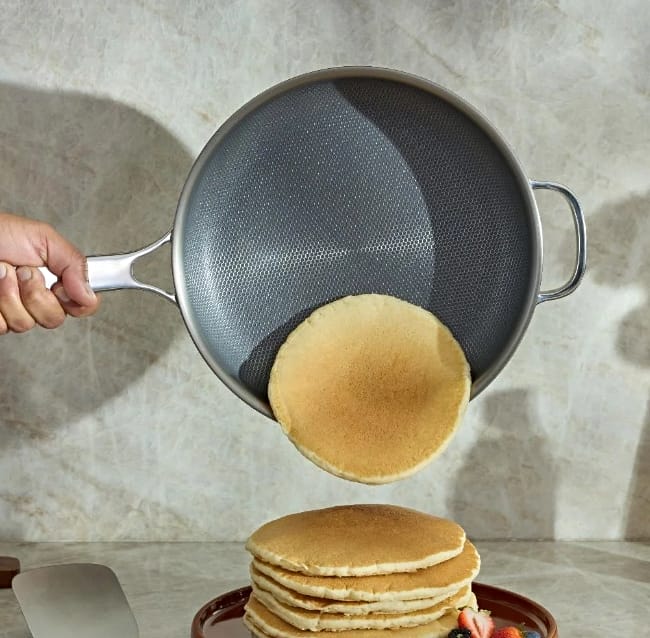Images of the titanium always pan pro held sideways with a pancake sliding out onto a stack of pancakes on plate