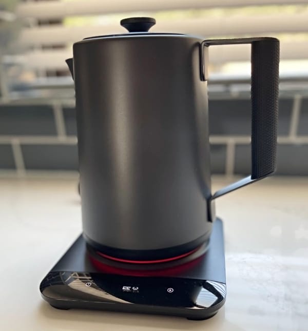 Saki-Luna-Pro-plastic-free-electric-tea-kettle sitting on an off-white table with a blue tile wall in the background