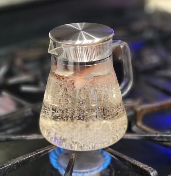 TeaBloom-glass-tea-kettle-no-plastic sitting over an active gas stove burner with water actively boiling